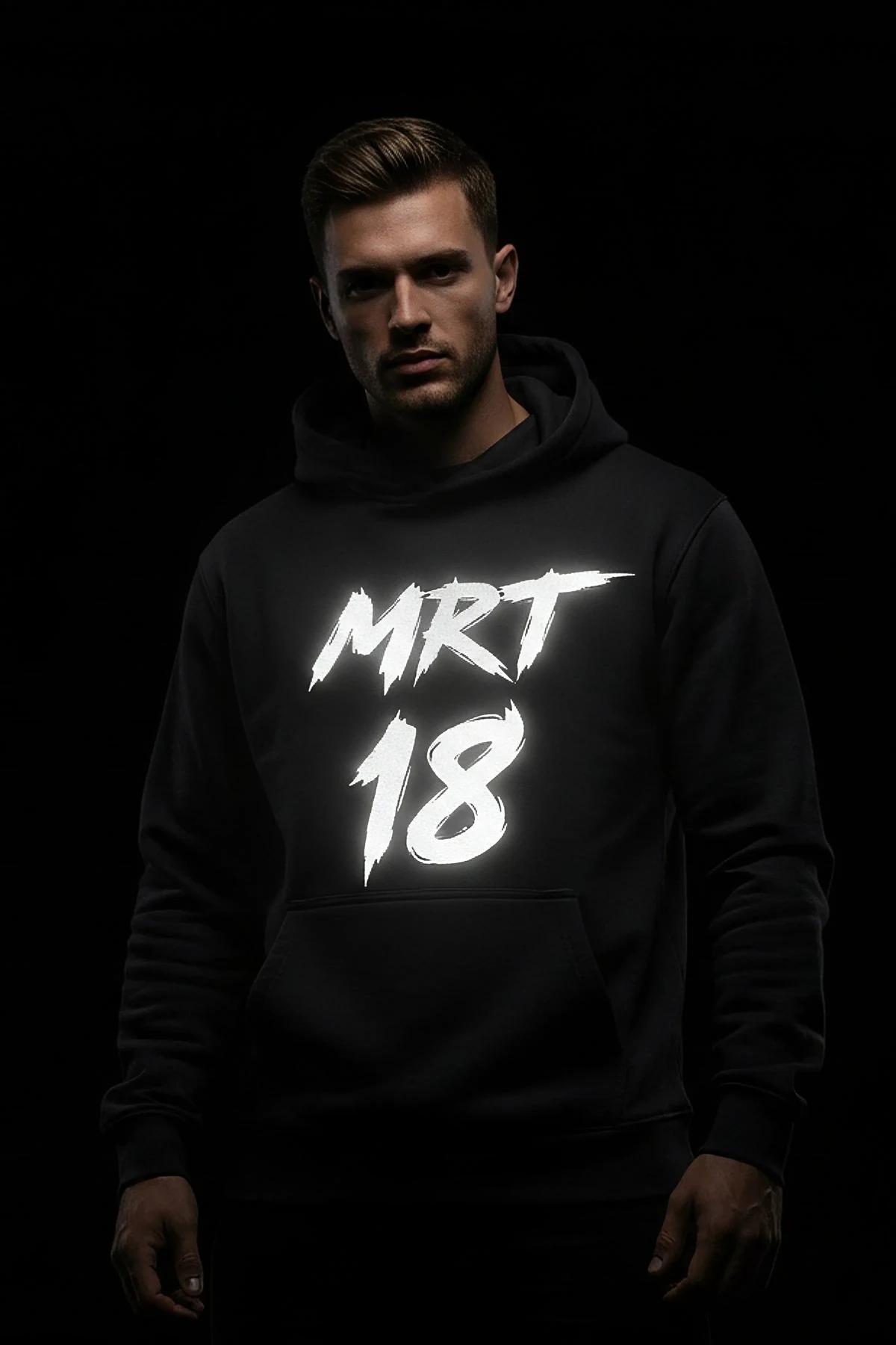 Reflective black pullover hoodie with large MRT 18 brushstroke graphic glowing white under flash light on male model