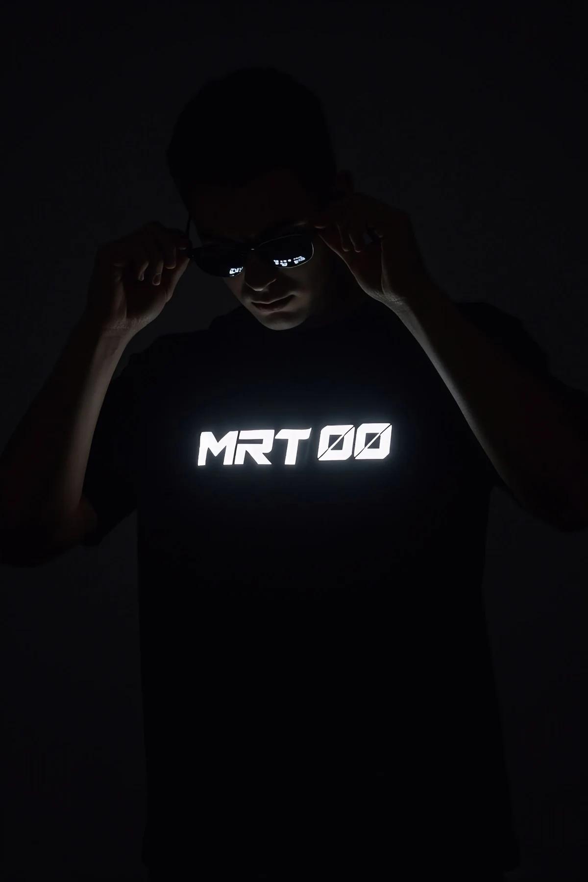 black oversized t-shirt with bright white reflective MRT 00 front print lit up in dark setting worn by male model