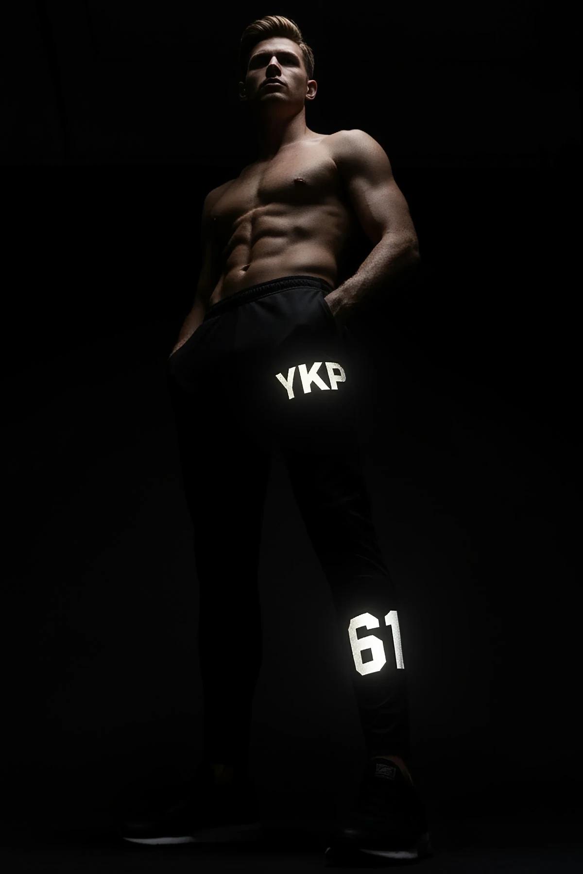 Black athletic leggings with white retroreflective YKP lettering at mid-thigh and 61 number at lower calf glowing under flash