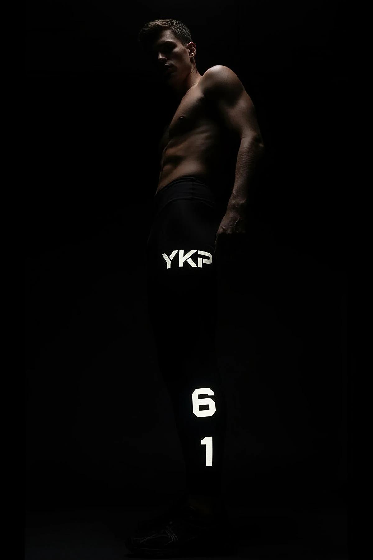 Close-up of white reflective YKP block print on black stretch-knit leggings under direct light