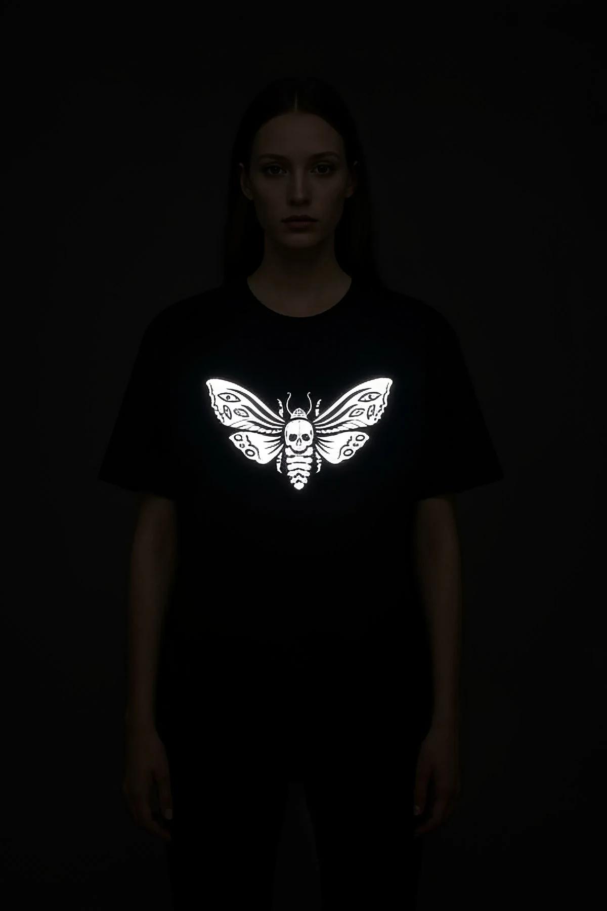 Death's head moth reflective print detail on black oversize t-shirt chest, skull face and wing veins visible