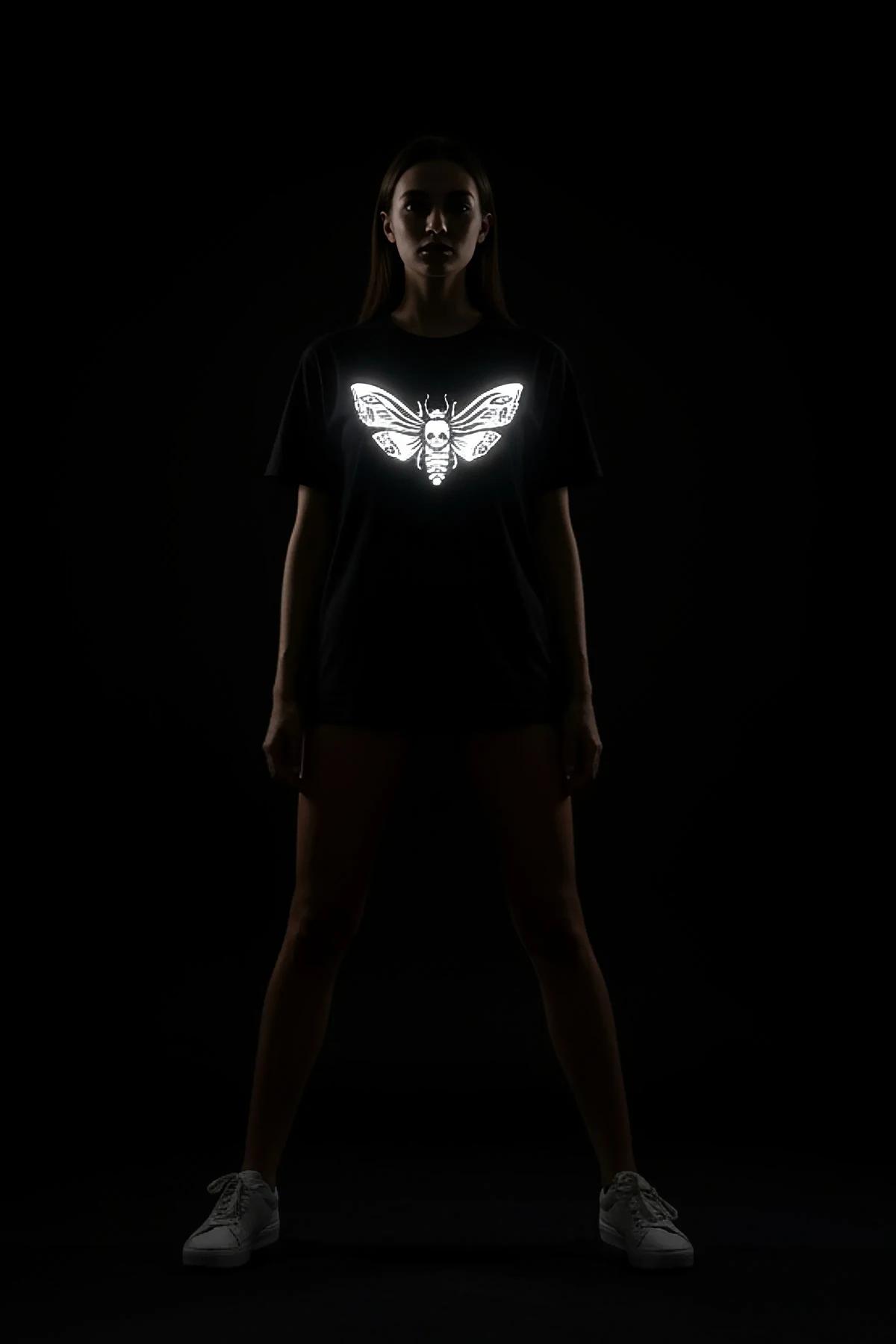 Black oversize graphic tee with large retroreflective moth spread-wing print, daytime tonal dark view