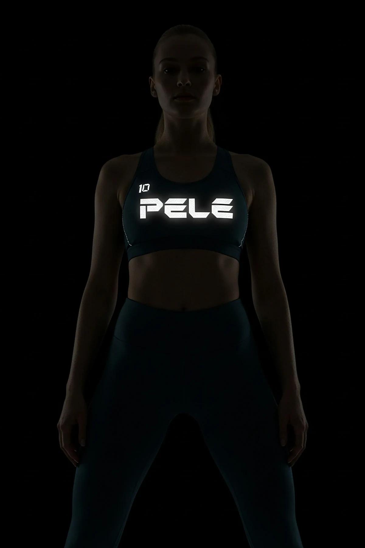 Black racerback sports bra with large white reflective PELE 10 front print glowing under direct light