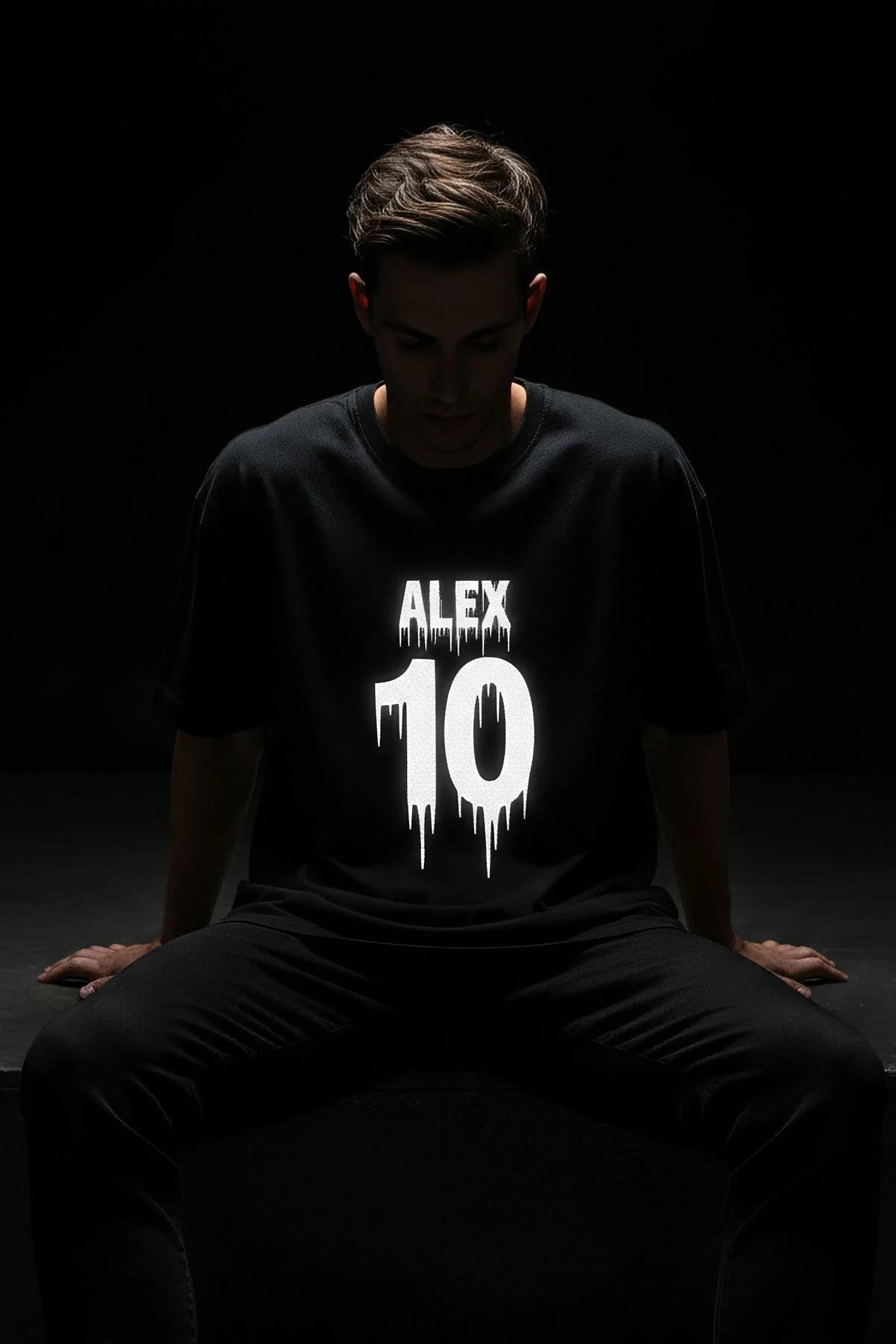 Reflective oversize black t-shirt with drip-style ALEX 10 white print glowing on front chest, worn by male model in low light