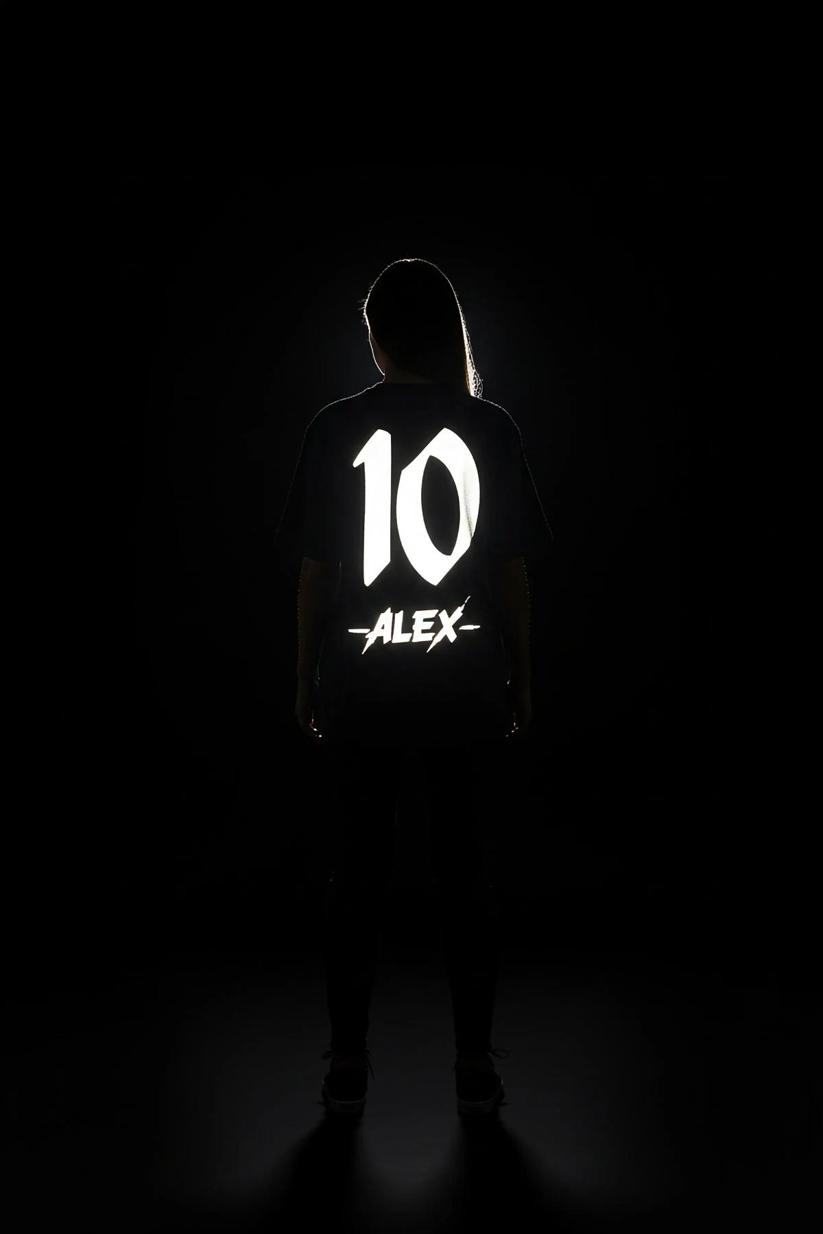 Back view of black oversized t-shirt showing full ALEX 10 reflective drip print panel under direct flash