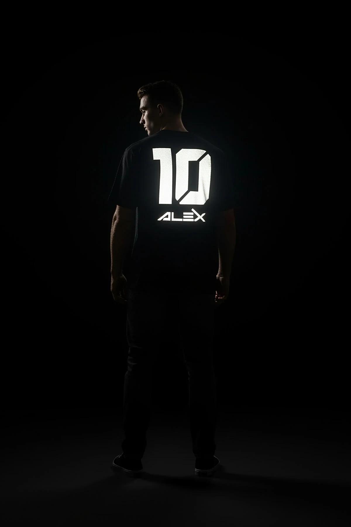 Close-up of retroreflective ALEX 10 drip lettering on black cotton jersey, white glow under light source