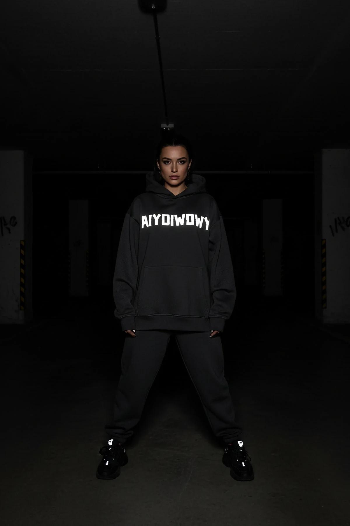 Reflective black oversized hoodie with AIYDIWDWY arch lettering glowing on front chest, worn with black joggers