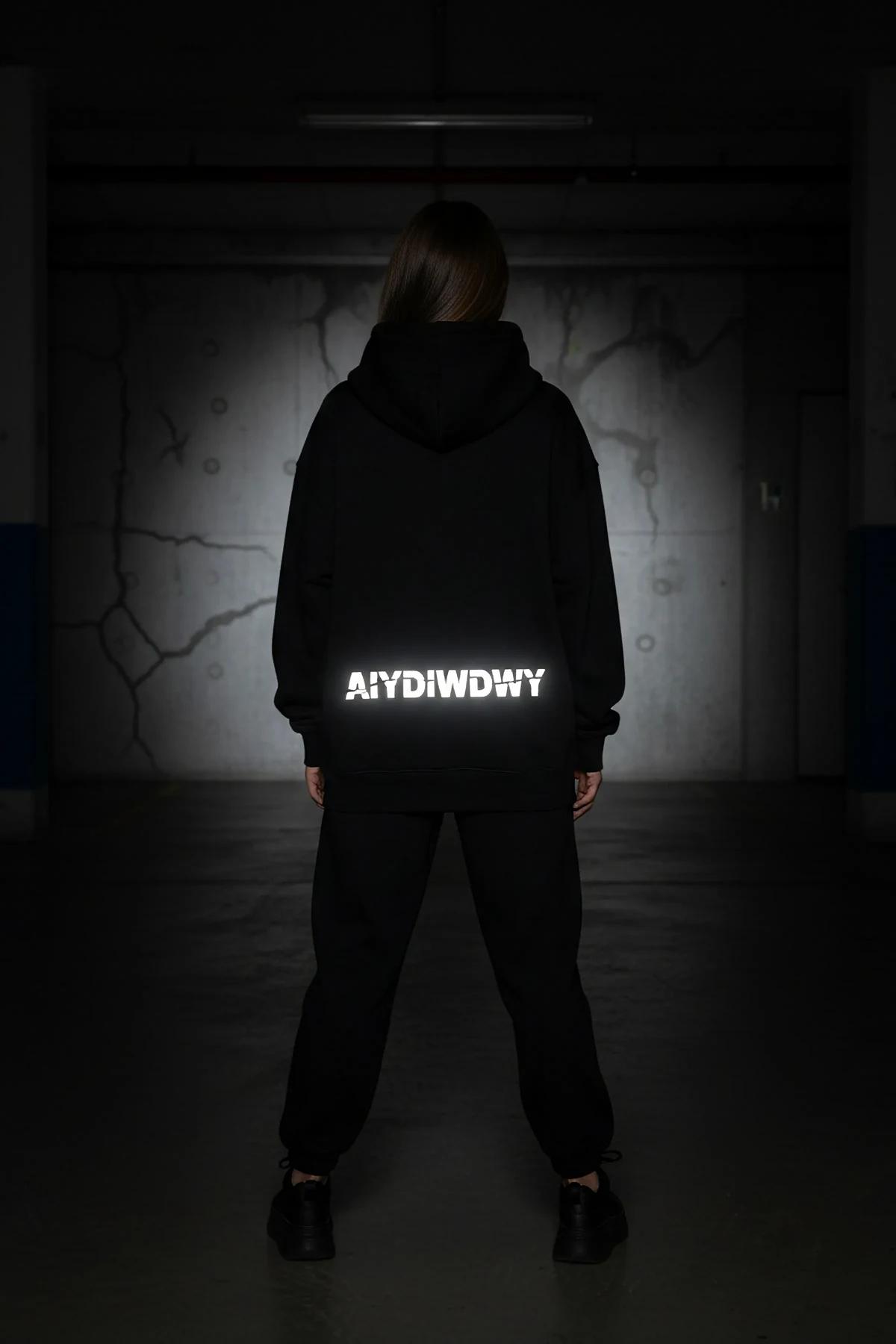 Back view of black oversized hoodie showing reflective AIYDIWDWY arch print activated under direct light