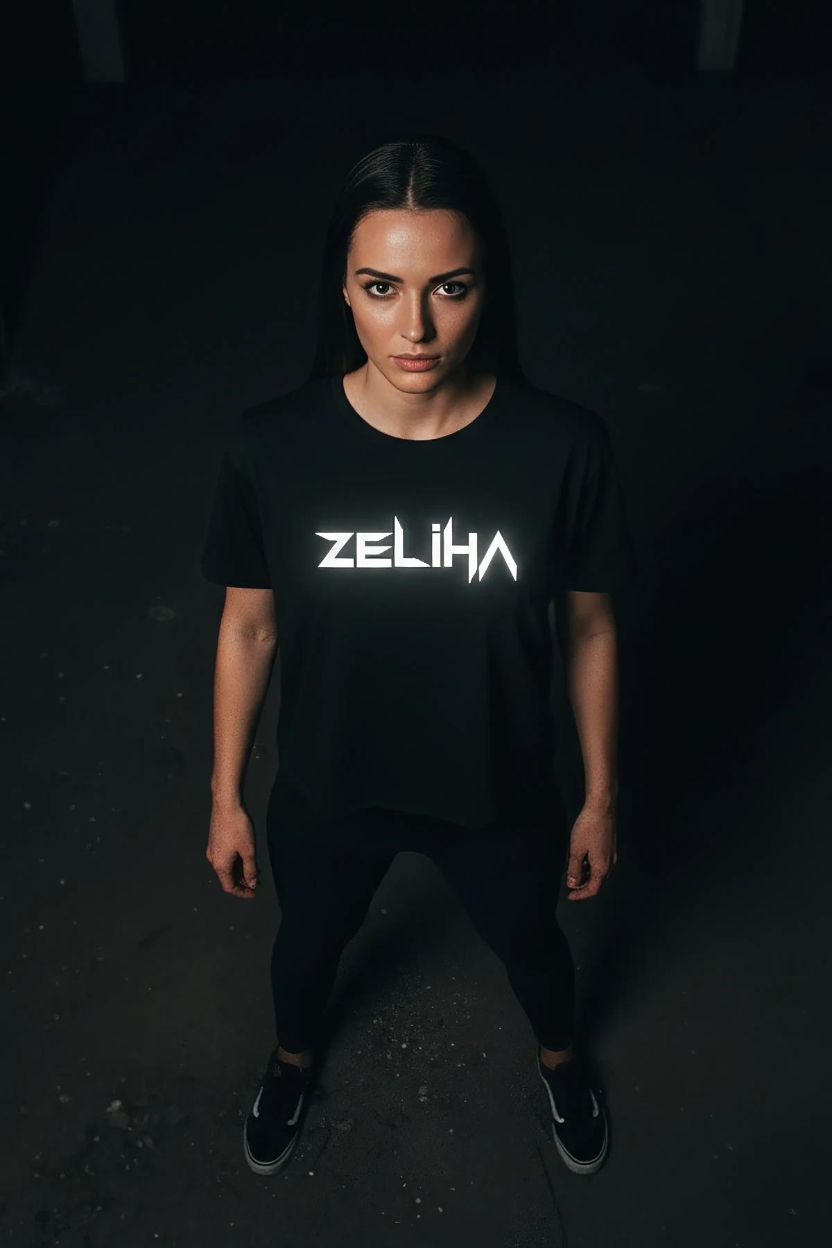 Black crop t-shirt with bright white reflective ZELIHA angular name print glowing on chest under direct light