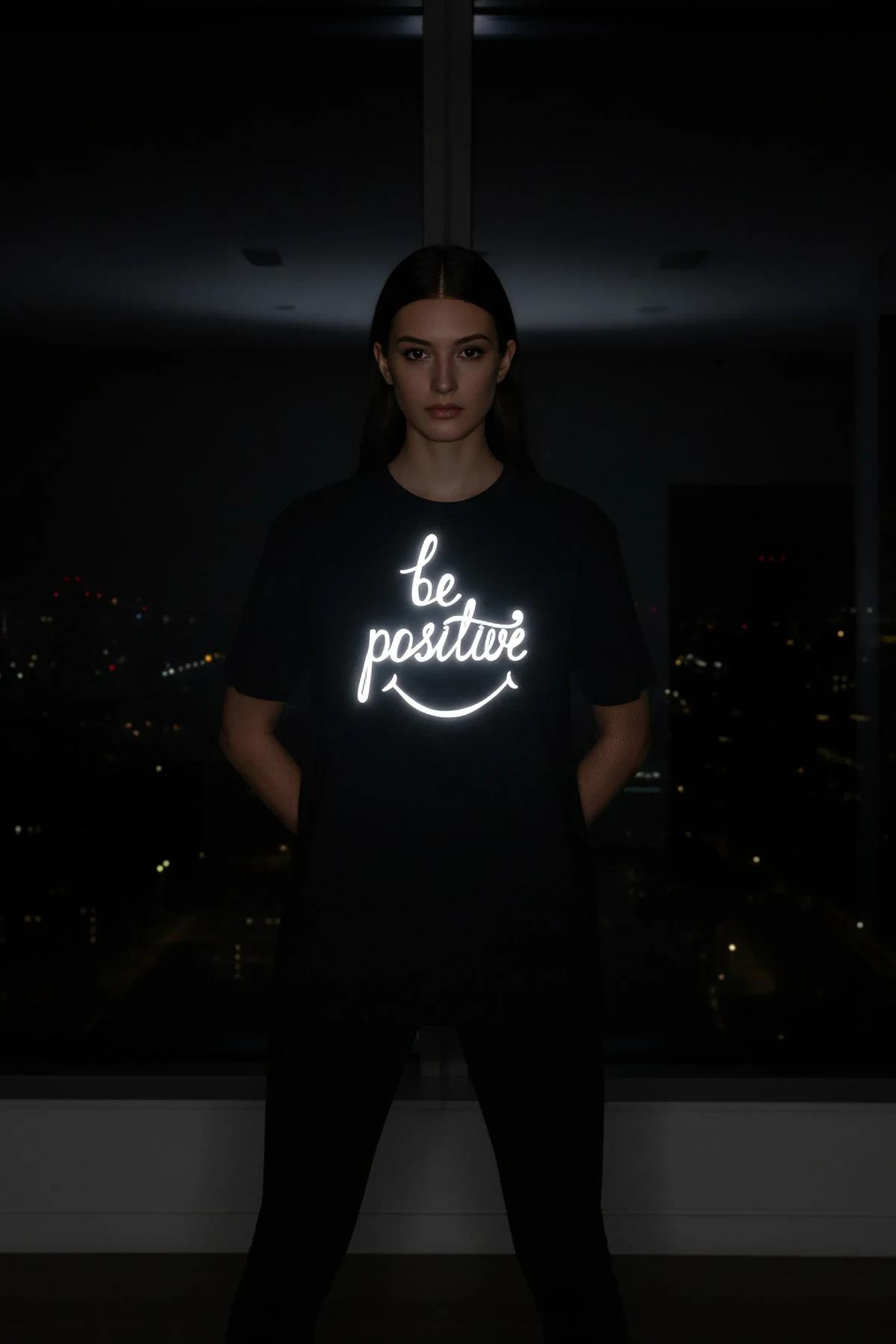 Reflective print oversize black t-shirt with glowing be positive script and smiley face on chest worn at night