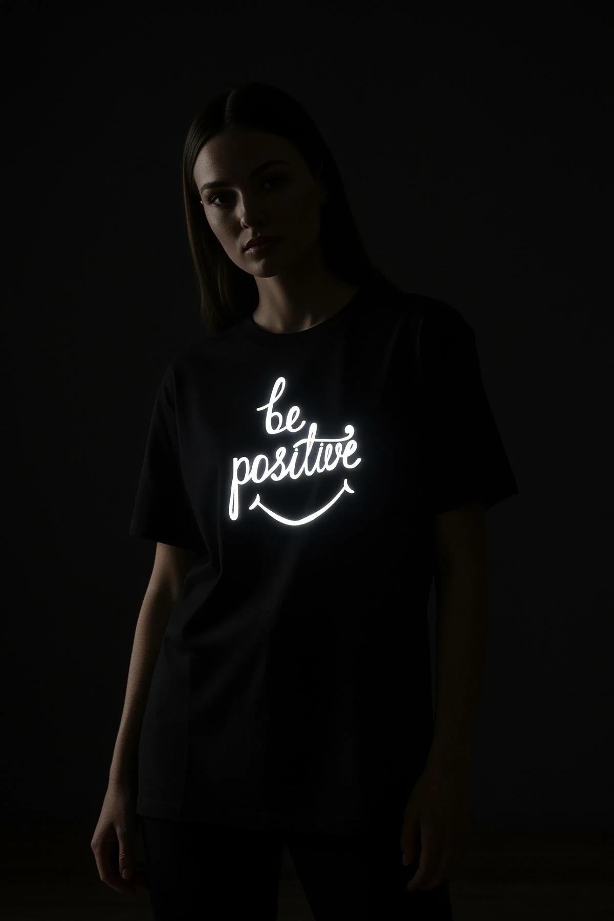 Close-up of retroreflective be positive cursive script print on black cotton-blend t-shirt chest