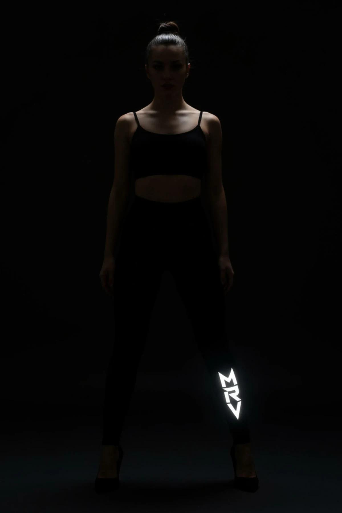black reflective leggings with vertically stacked MRV letter print glowing white on lower left leg against dark background