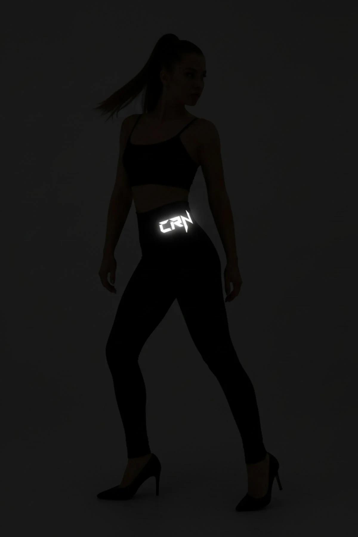 Black reflective leggings with CRN waistband print glowing white in darkness, full-length activewear