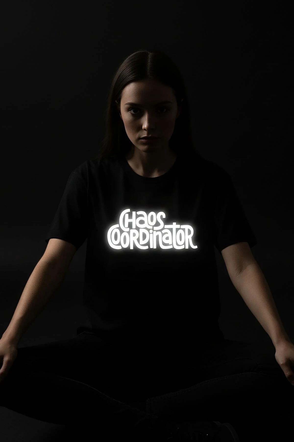 CHAOS COORDINATOR retroreflective chest print on black oversize t-shirt photographed under camera flash