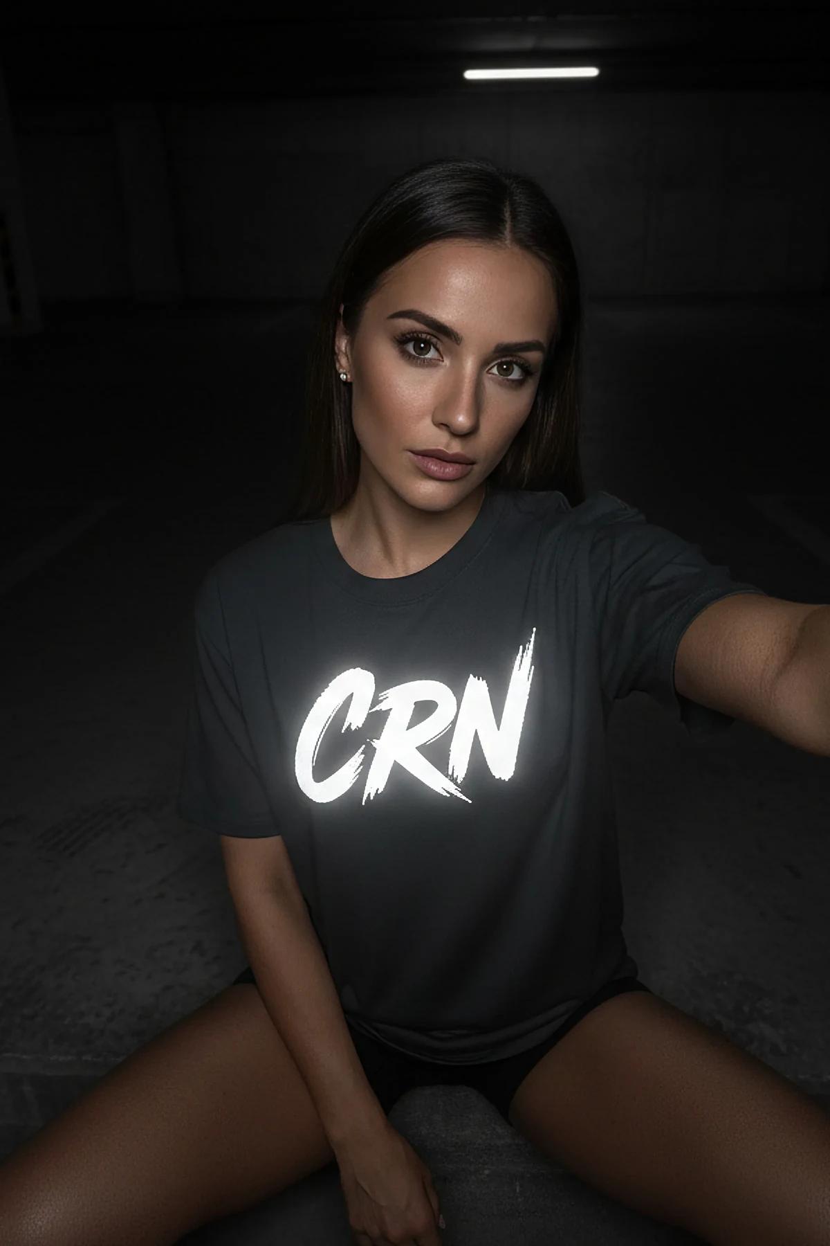 black oversized t-shirt with reflective CRN brush-script front print glowing white under flash photography