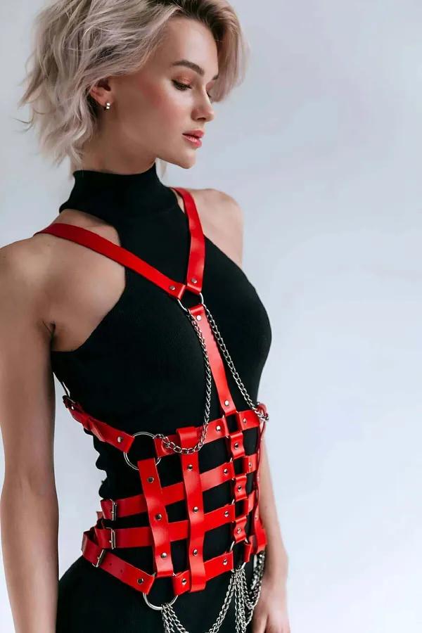 Red faux leather strappy body harness with cage-grid waist panel, silver O-rings and draped chain detail worn over black turt