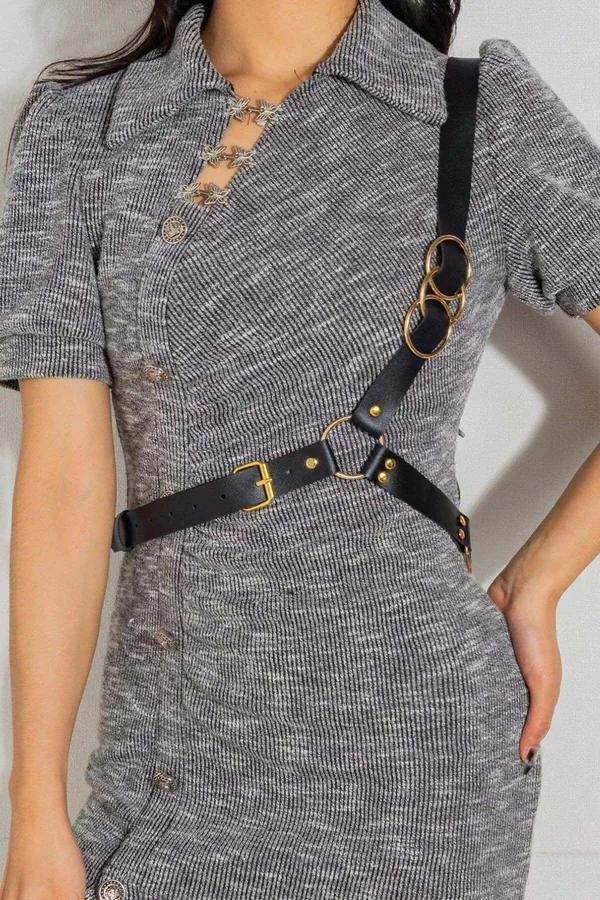 Black faux leather chest harness with three gold O-rings and adjustable buckle straps worn over gray knit dress