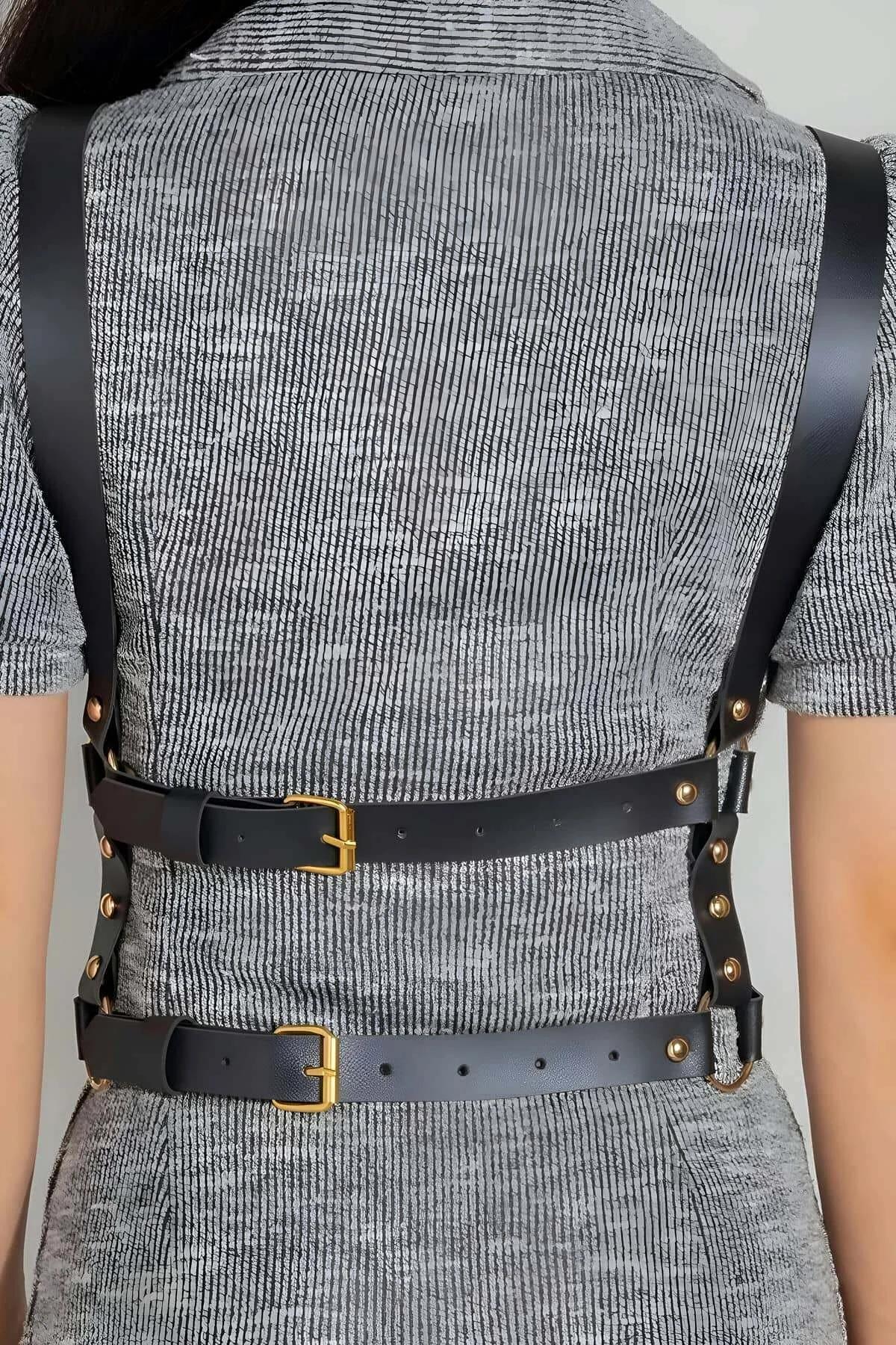 close-up of gold-tone O-ring and buckle hardware on black faux leather X-strap harness