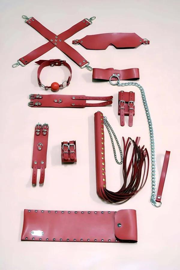 Red vegan leather 9-piece accessory set with hogtie straps, wrist ankle cuffs, blindfold, waist belt, and flogger laid flat