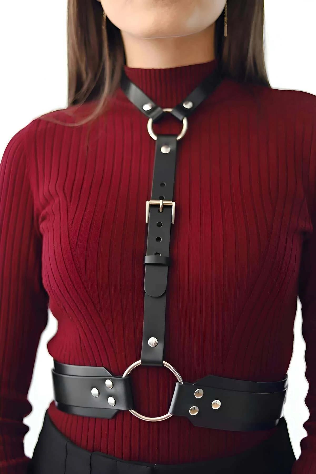 Black vegan leather chest harness strap with collar-level O-ring, layered over fitted knit top