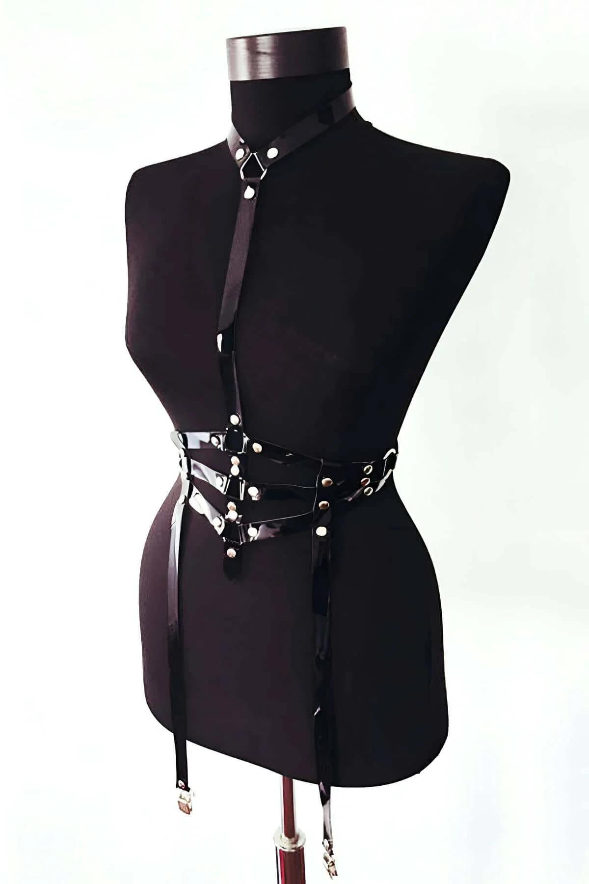 front view black PU harness showing crossed V-strap waist panel with silver stud closures and D-ring anchors