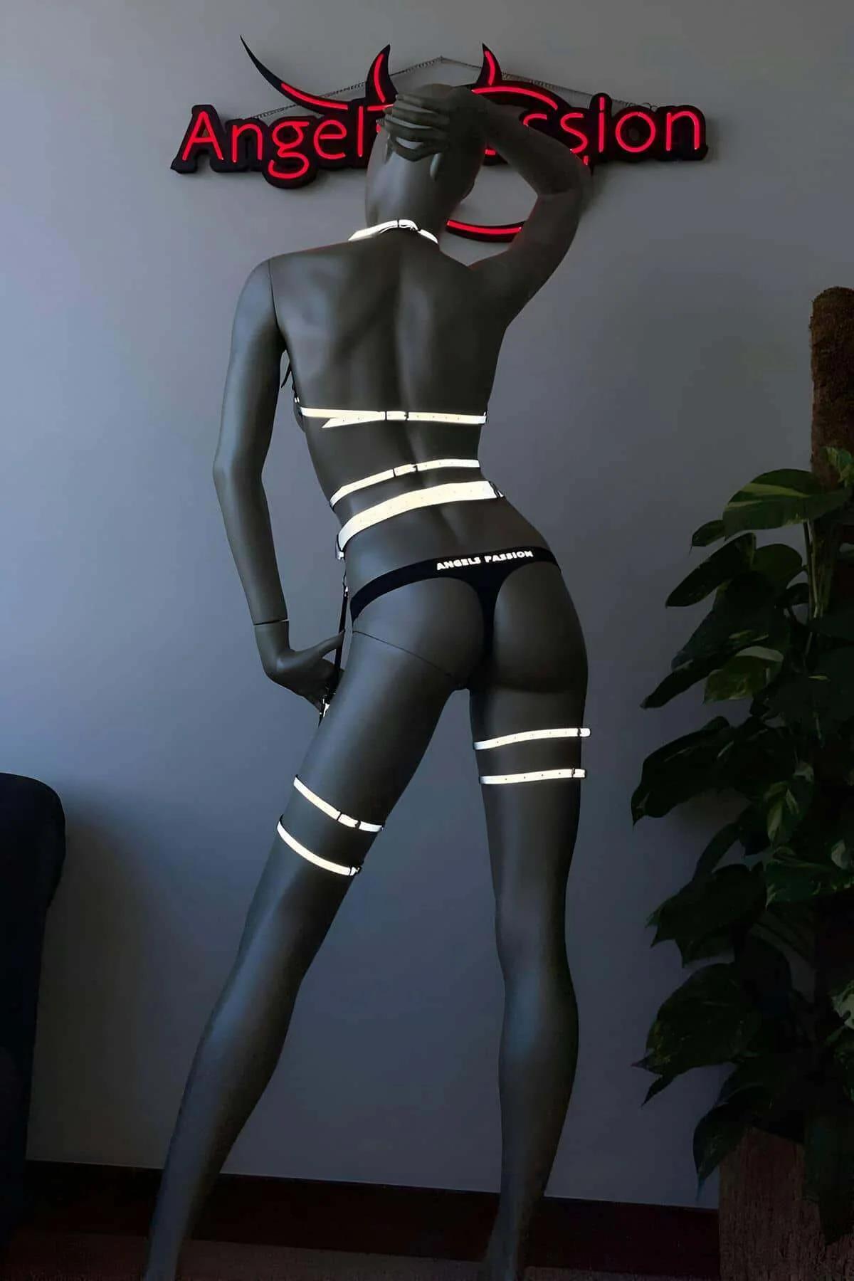 Full body side view of reflective holographic three-piece harness set glowing bright white under stage spotlight