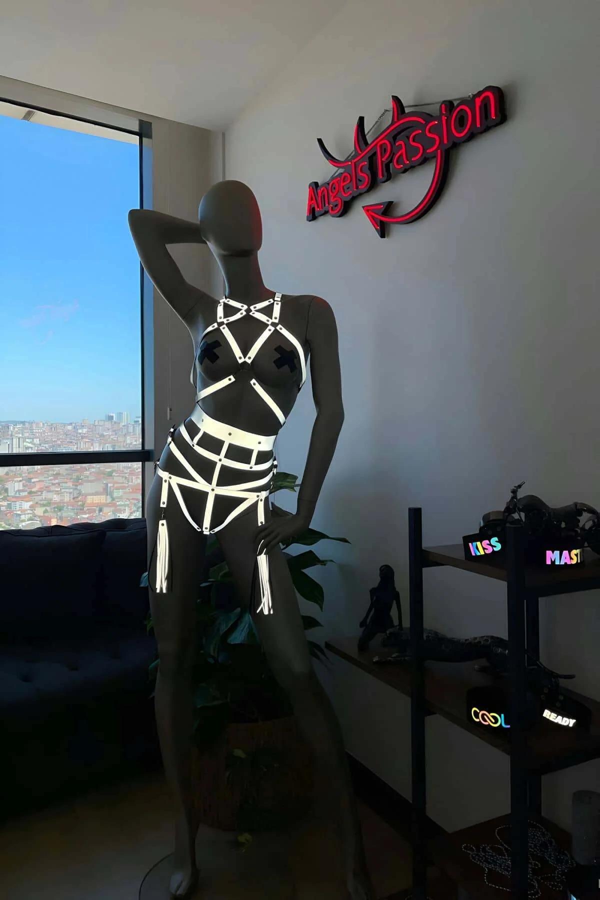Full front view of white reflective multi-strap body harness glowing under dim light against dark background