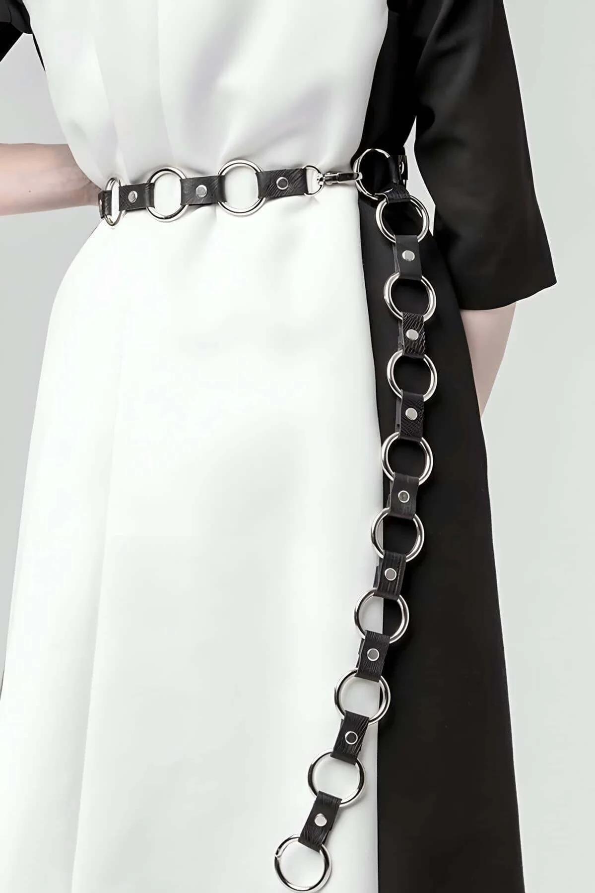 Black faux leather belt with cascading silver O-ring chain drop worn over white midi dress at waist