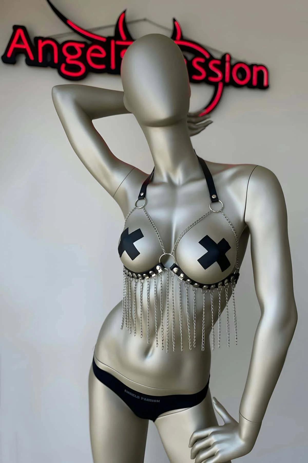 Close-up of silver fringe chains draped from black faux leather bra harness lower band with flat-head stud detail