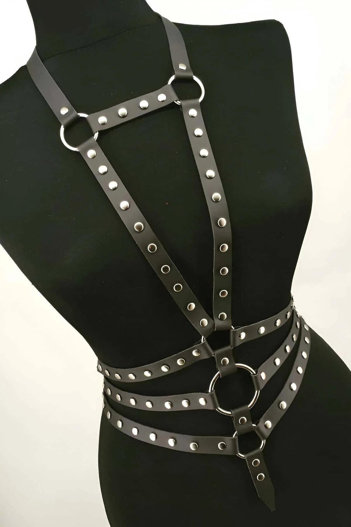 Studded faux leather harness layered over black mini skirt showing full torso coverage and strap layout