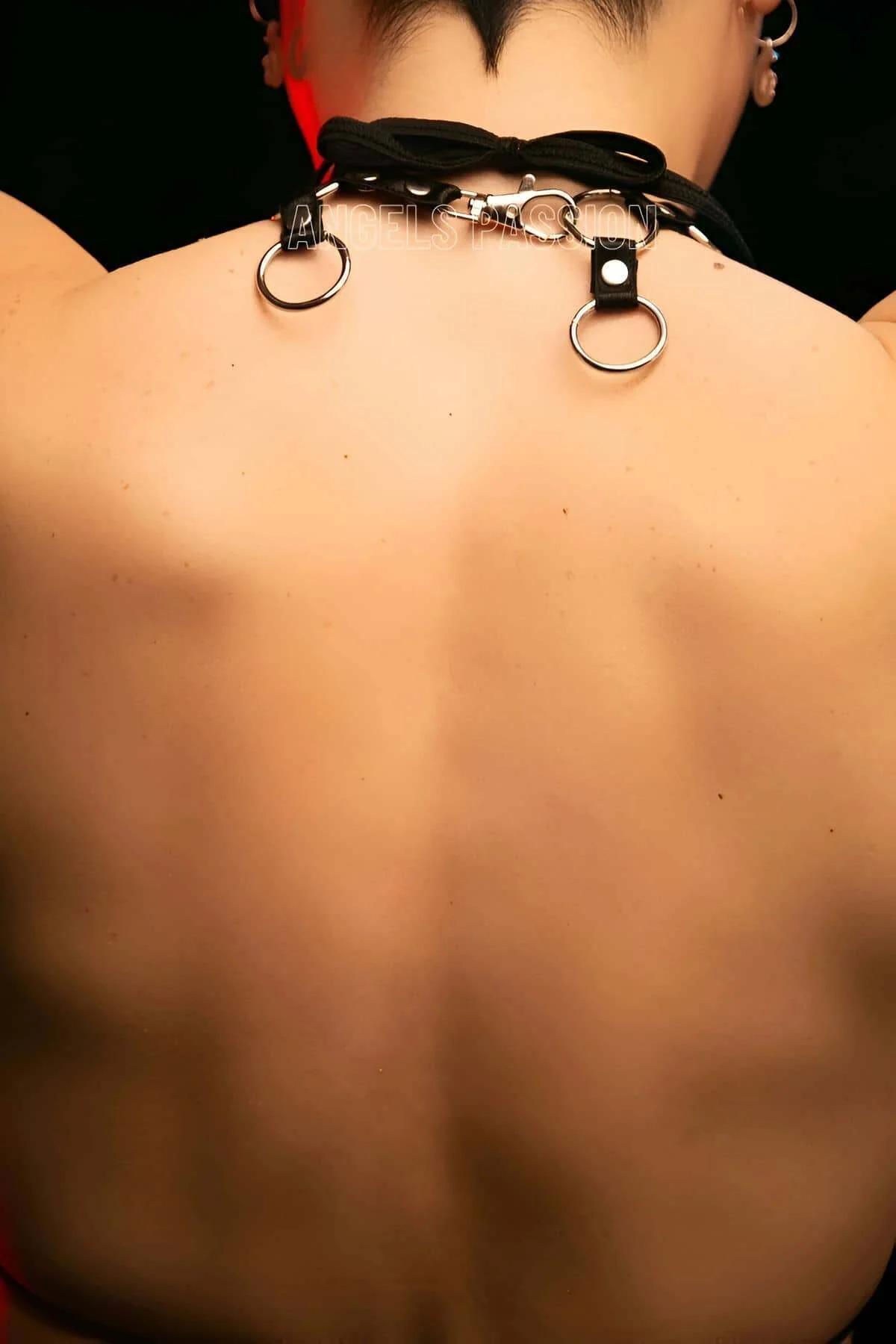 Side angle of black choker harness with silver O-rings worn over bare skin