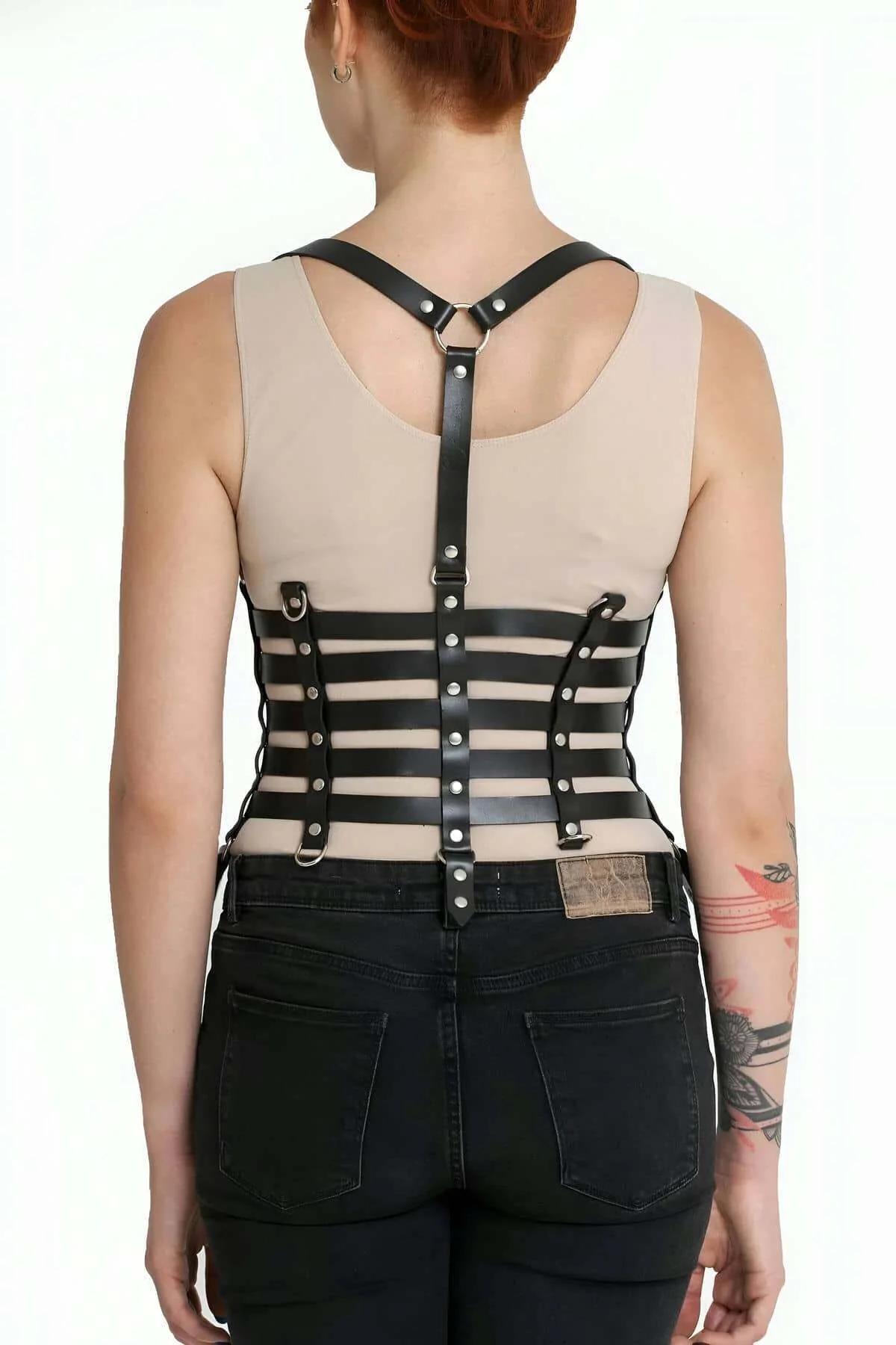 black five-band corset harness with D-rings worn over black jeans and beige top, side angle