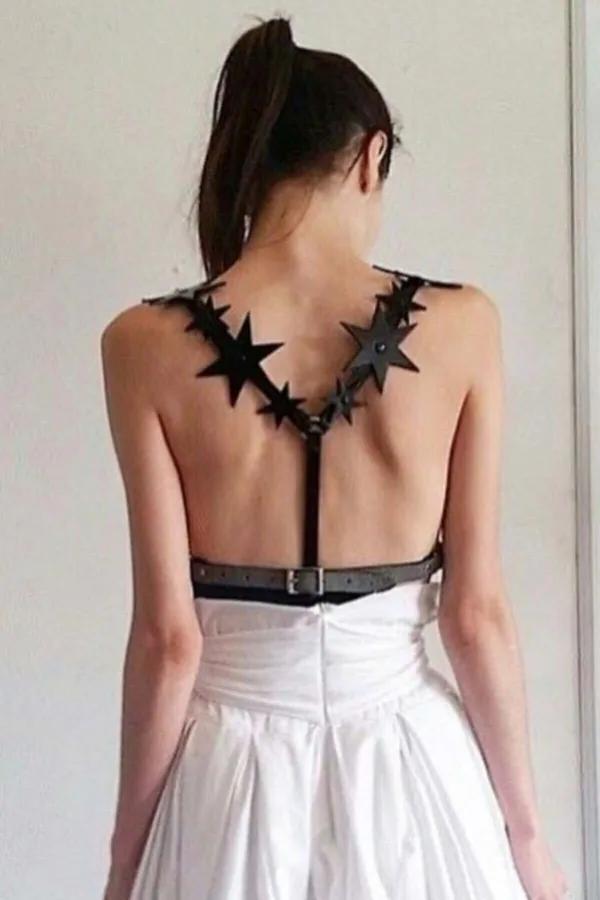 Black faux leather body harness with six-point star cutouts across upper back and adjustable studded waist belt, rear view