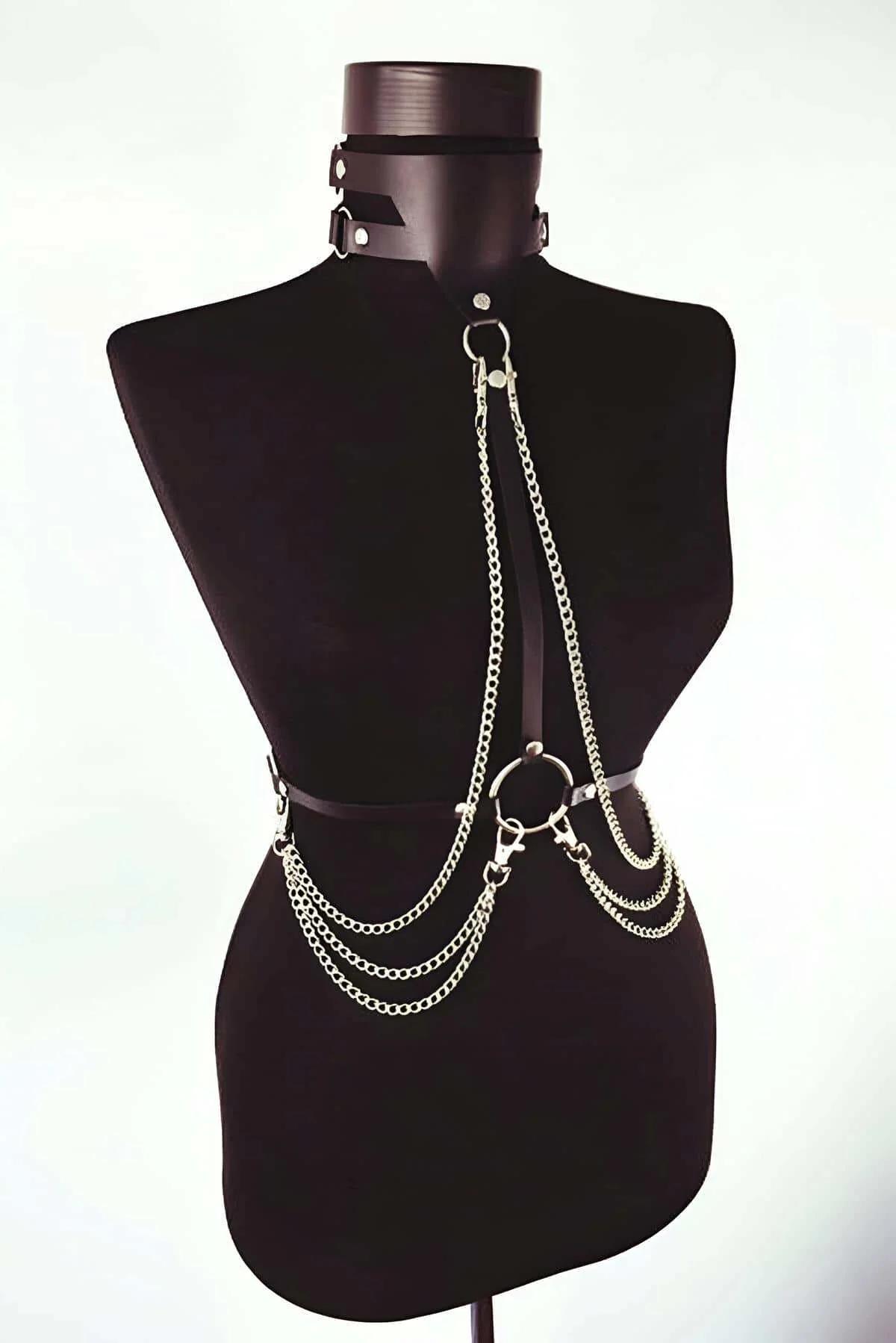 Close-up of silver O-ring anchor and curb-link chain cascade on black faux leather chest harness