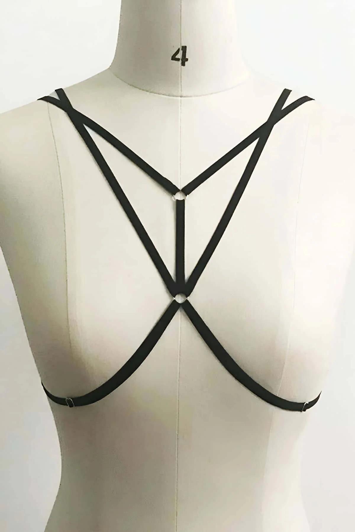 Close-up of silver O-ring hardware at center junction of black elastic nylon straps on body harness