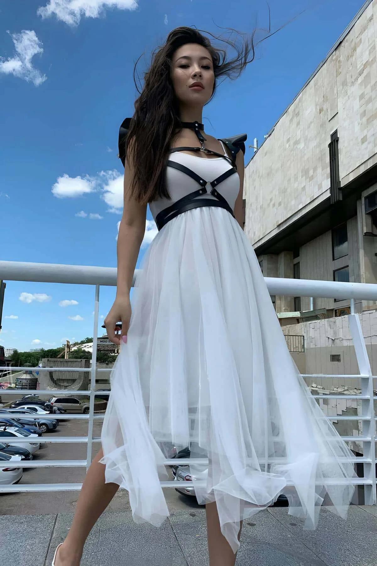 black strappy body harness with wide shoulder caps layered over white midi dress outdoors