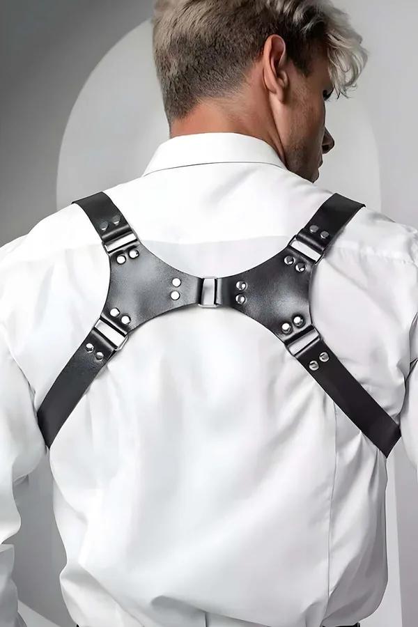 Black faux leather adjustable shoulder harness with silver buckles and rivets worn over a white dress shirt, back view
