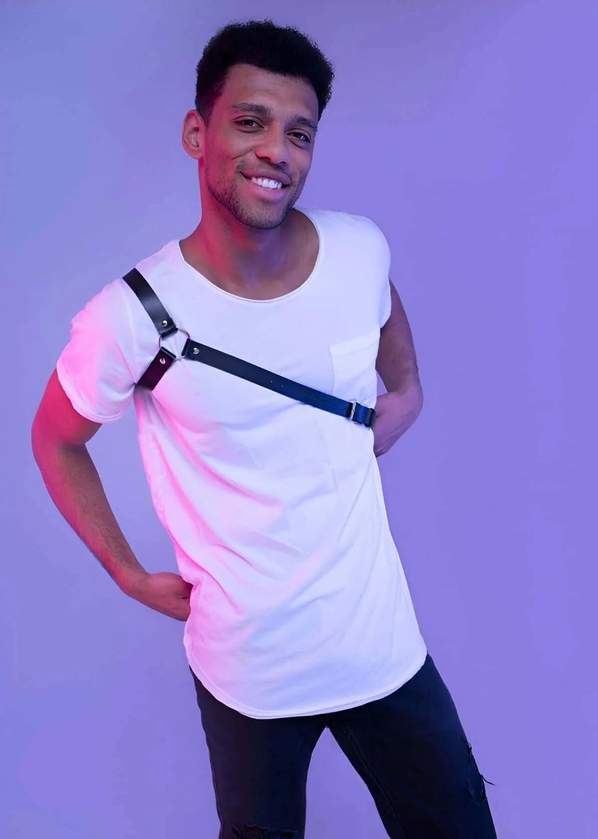 Black faux leather single shoulder body harness with silver O-ring worn diagonally across chest over white t-shirt