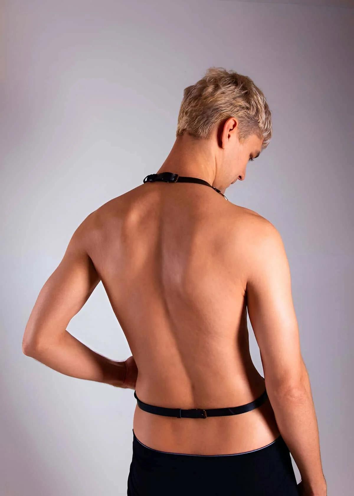 Close-up of gold-tone rectangular buckle detail on black faux leather diagonal chest strap