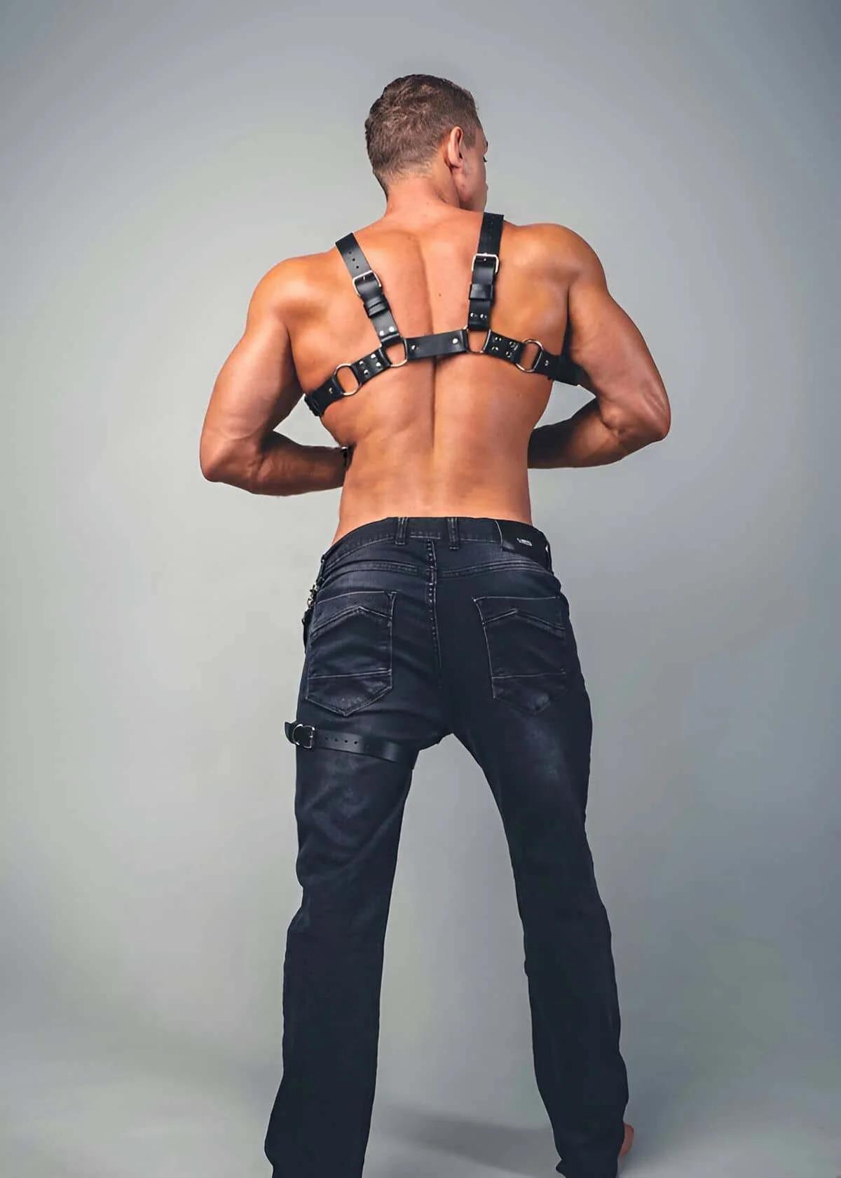 close-up of black faux leather chest harness showing central silver O-ring and stud-row connector panel