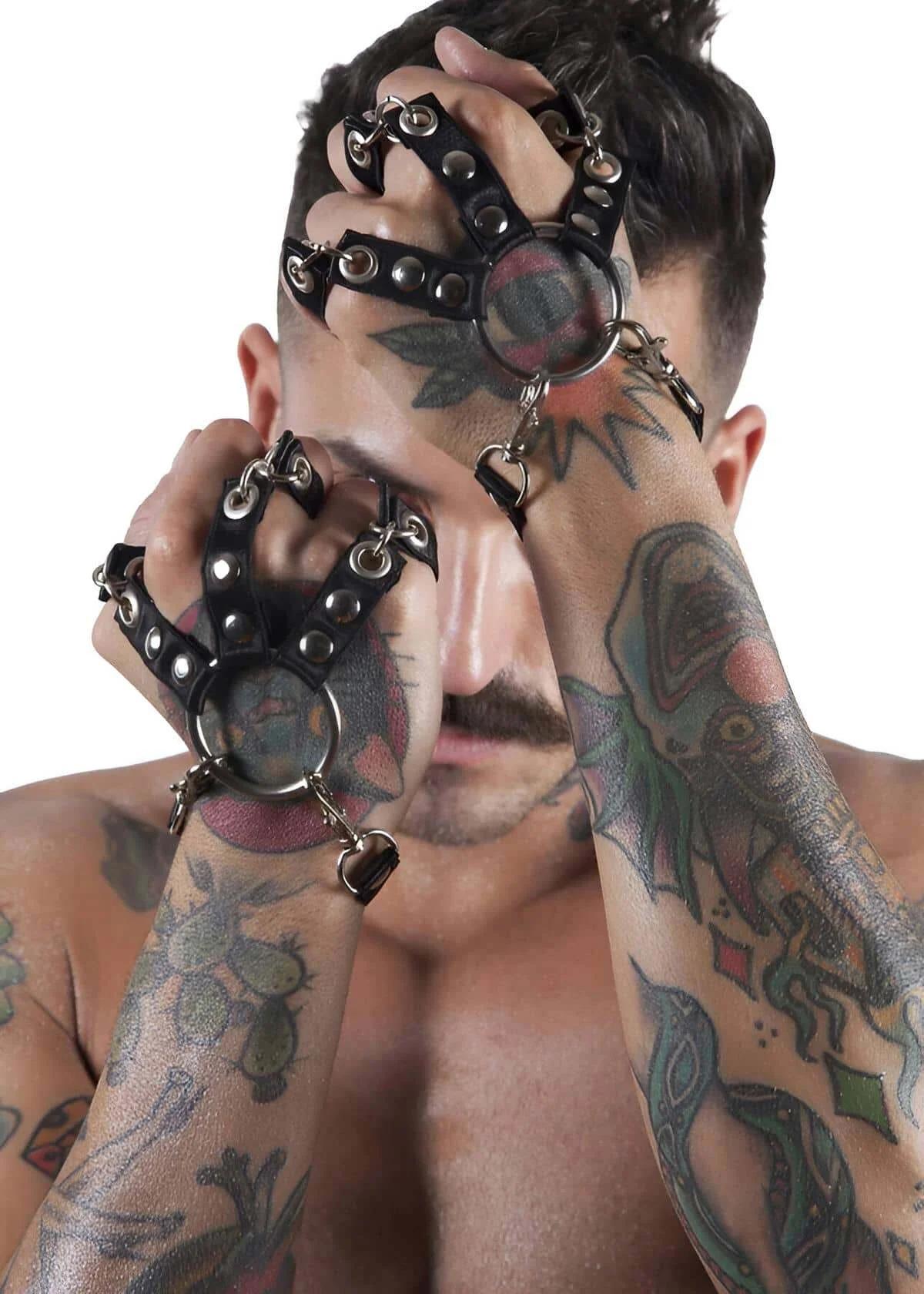 Black faux leather hand harness with silver O-ring at palm and dangling heart charm on tattooed male model