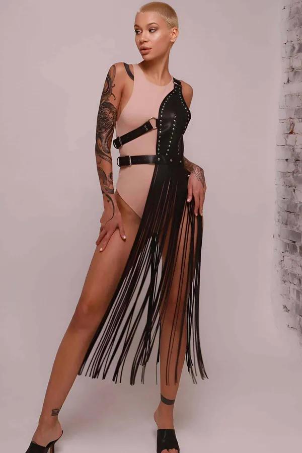 Black faux leather asymmetrical fringe harness skirt with silver stud trim and side buckle, worn over a nude bodysuit