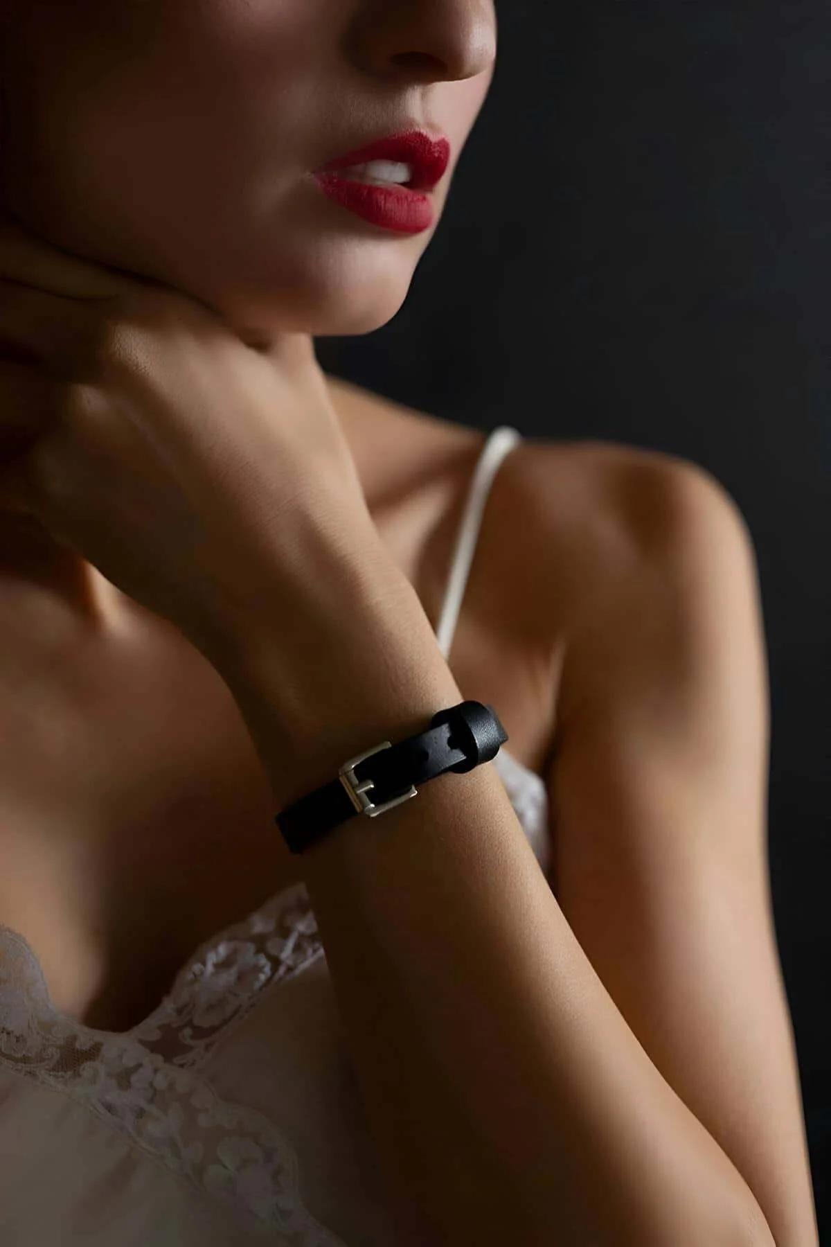 Black faux leather bracelet with gold-tone buckle worn on wrist, slim 1 cm band, smooth finish