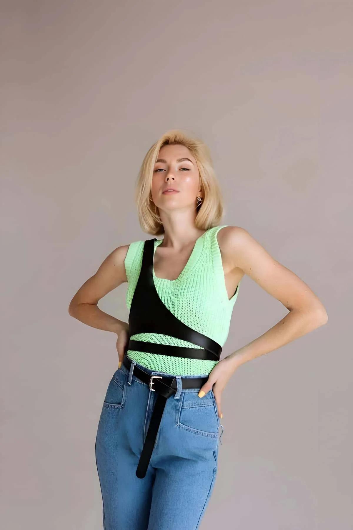 Black faux leather chest harness with diagonal shoulder strap and silver buckle worn over mint green knit top