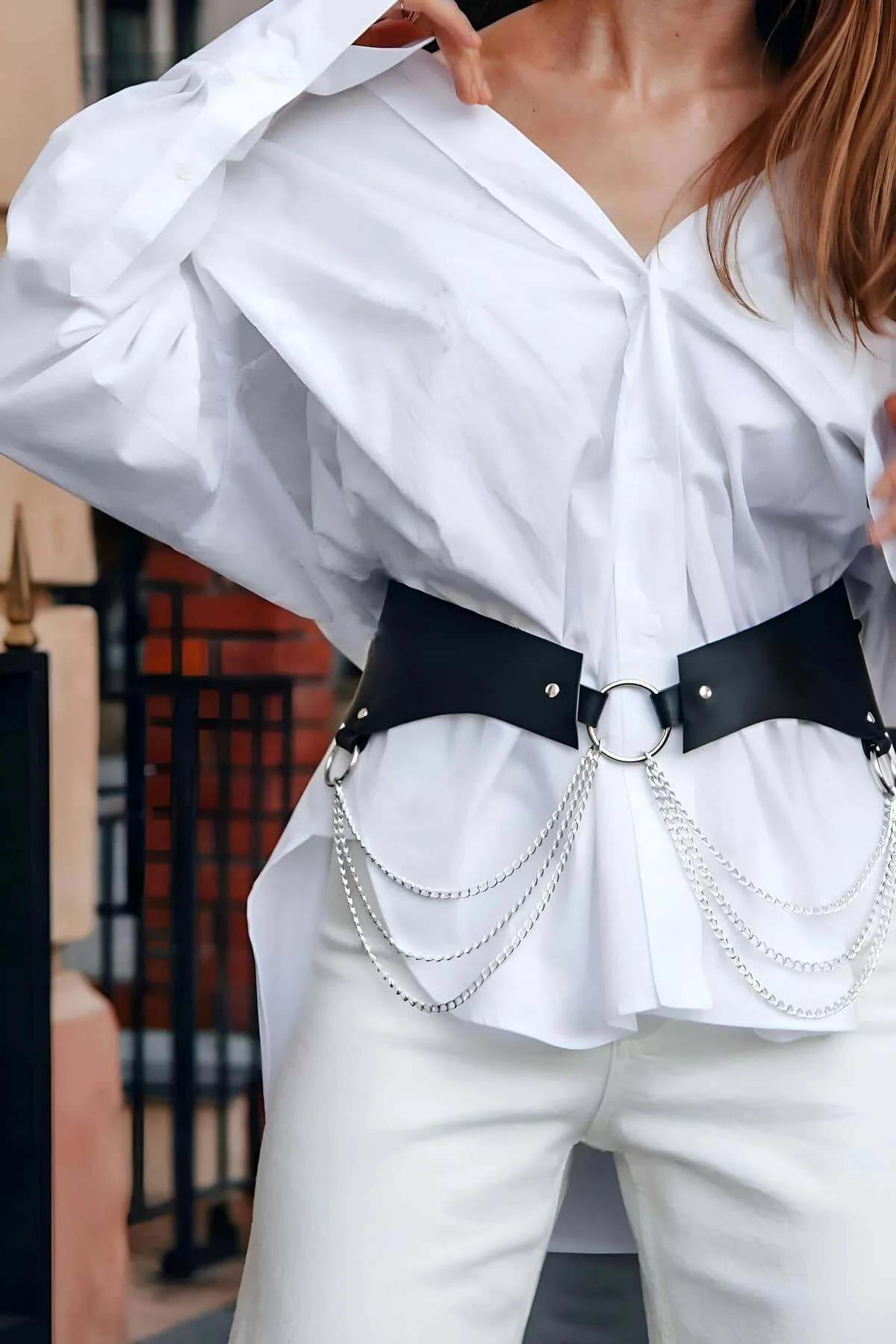 Black wide faux leather waist harness belt with silver O-ring center and layered chain drapes worn over white shirt