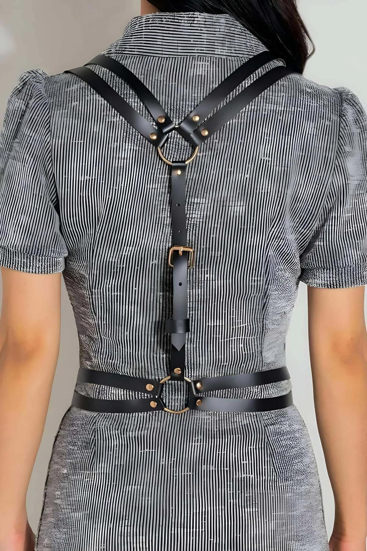Black faux leather strappy body harness with gold-tone O-ring at upper back and adjustable waist band, worn over striped shir
