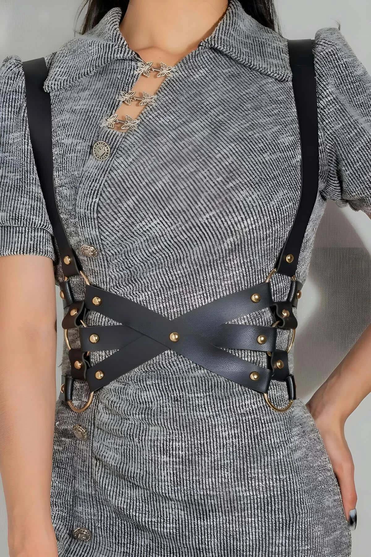 black faux leather X-strap body harness with gold O-ring hardware worn over gray knit dress