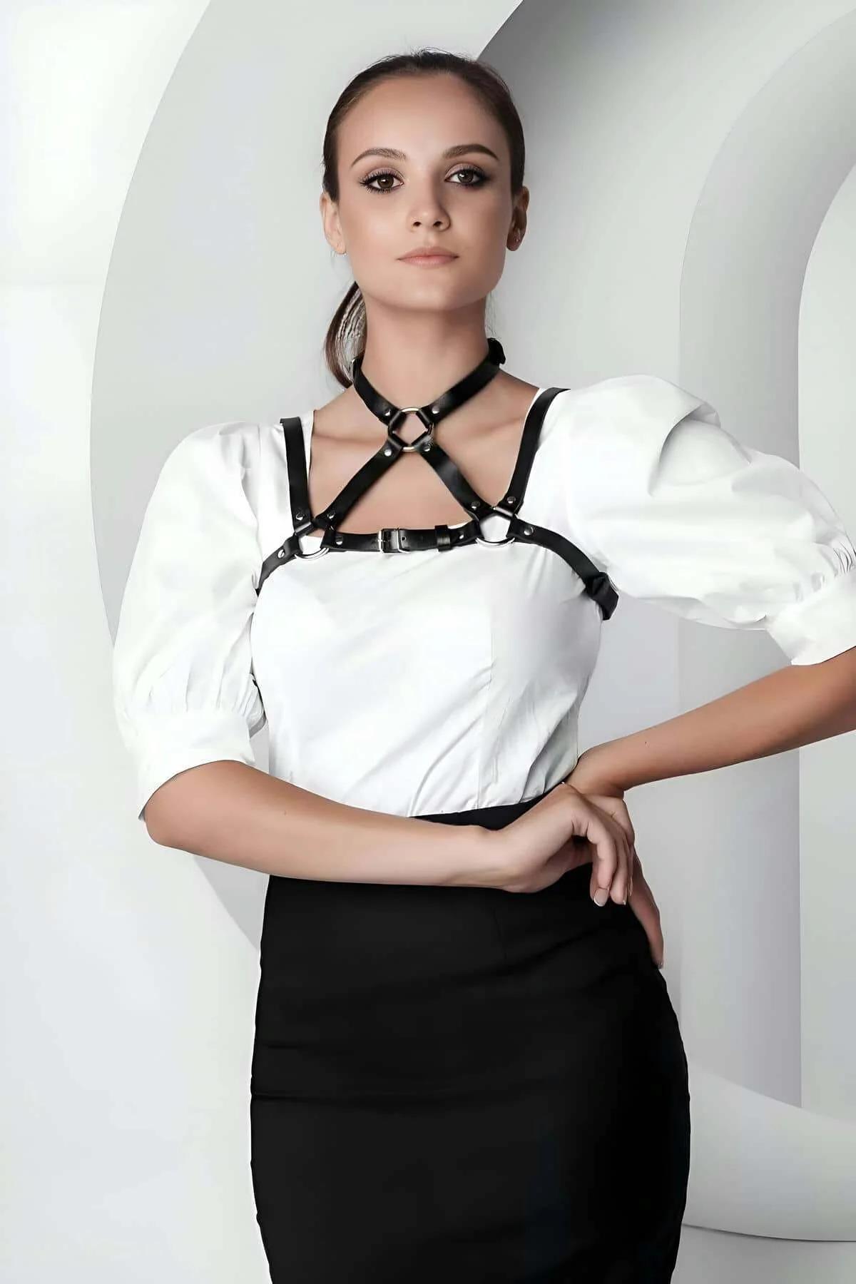 Black faux leather strappy O-ring chest harness with silver hardware worn over white blouse