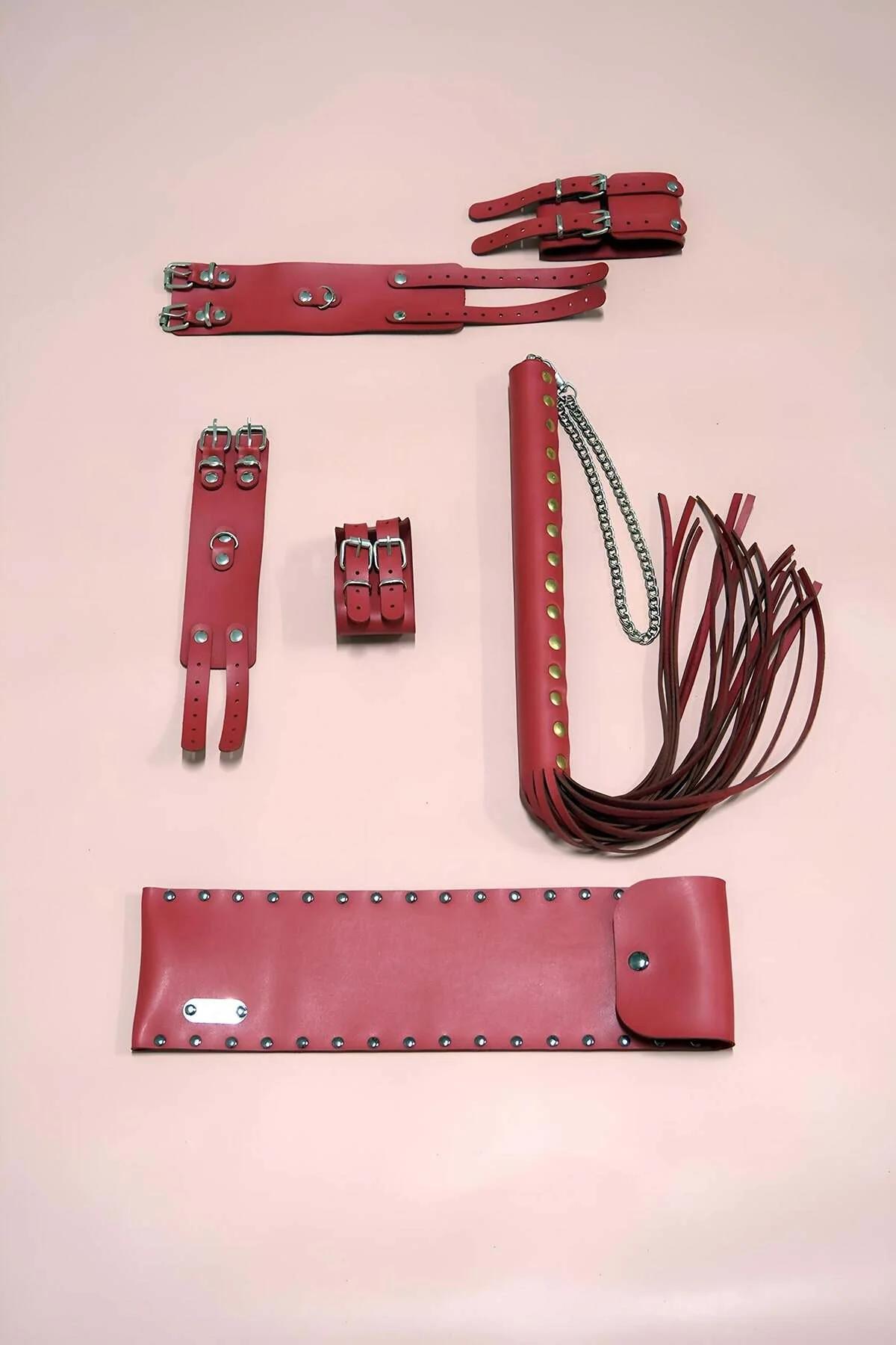 Red vegan leather accessory set with wide studded belt, double-buckle wrist cuffs with silver D-rings, and multi-tassel flogg