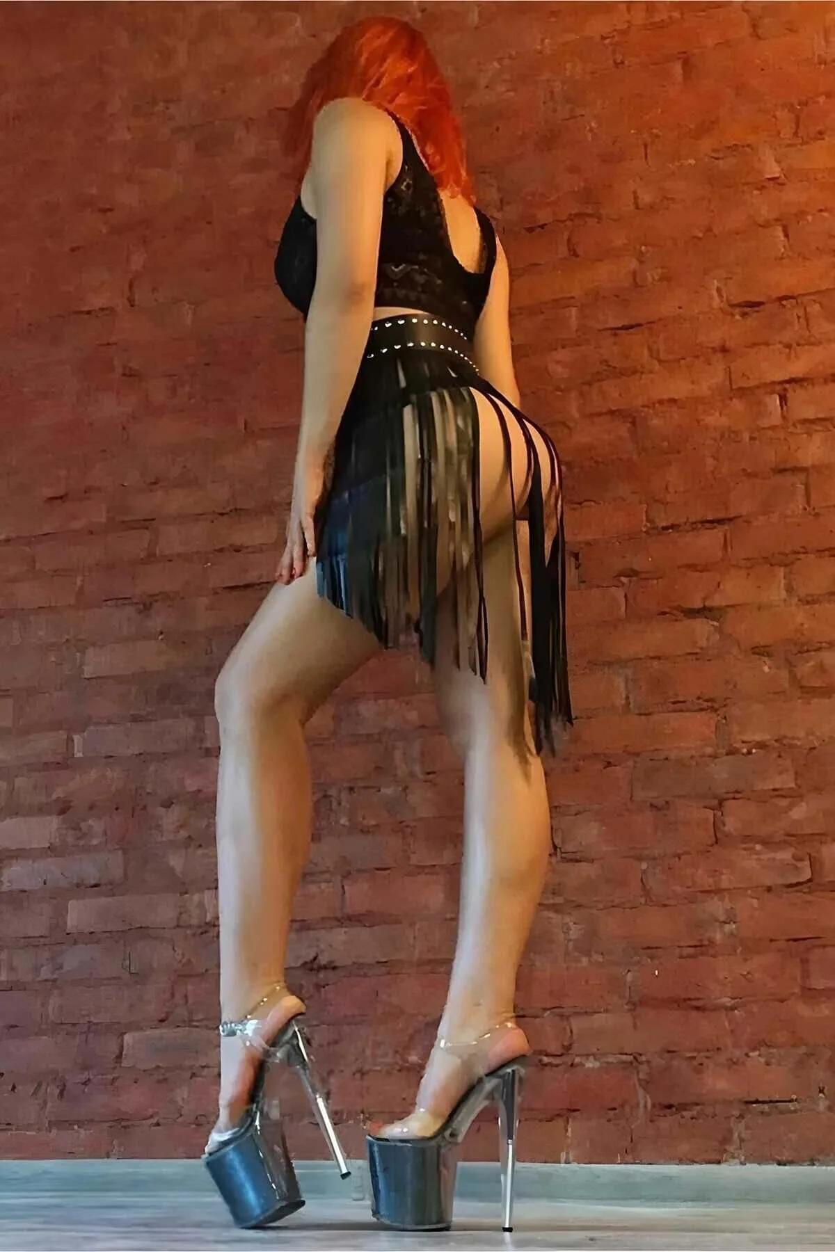 Black faux leather fringe hip belt skirt with silver stud waistband, long fringe strips at mid-thigh length, back view